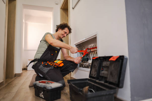 A person in overalls crouches in the hallway, expertly working with a wrench on the HVAC system of a home. Surrounded by toolboxes, they adjust pipes or valves inside a wall cabinet, ensuring everything is in prime condition for seamless property management.